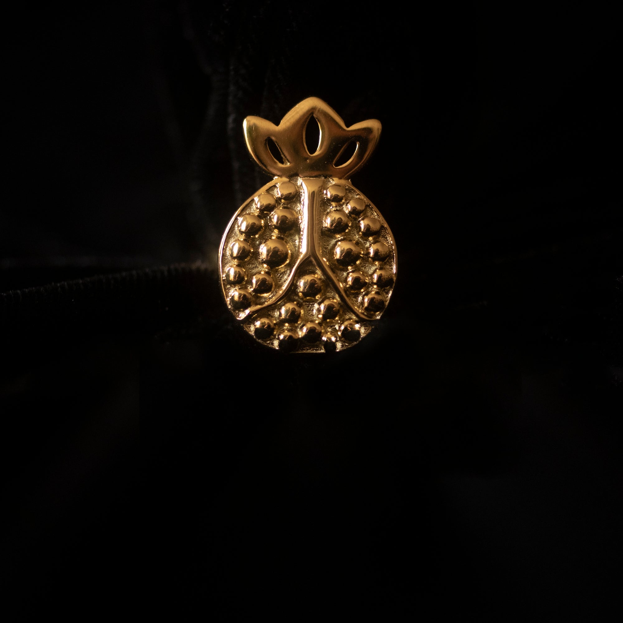 Against a black backdrop sits a pomegranate shaped gold ring. 
