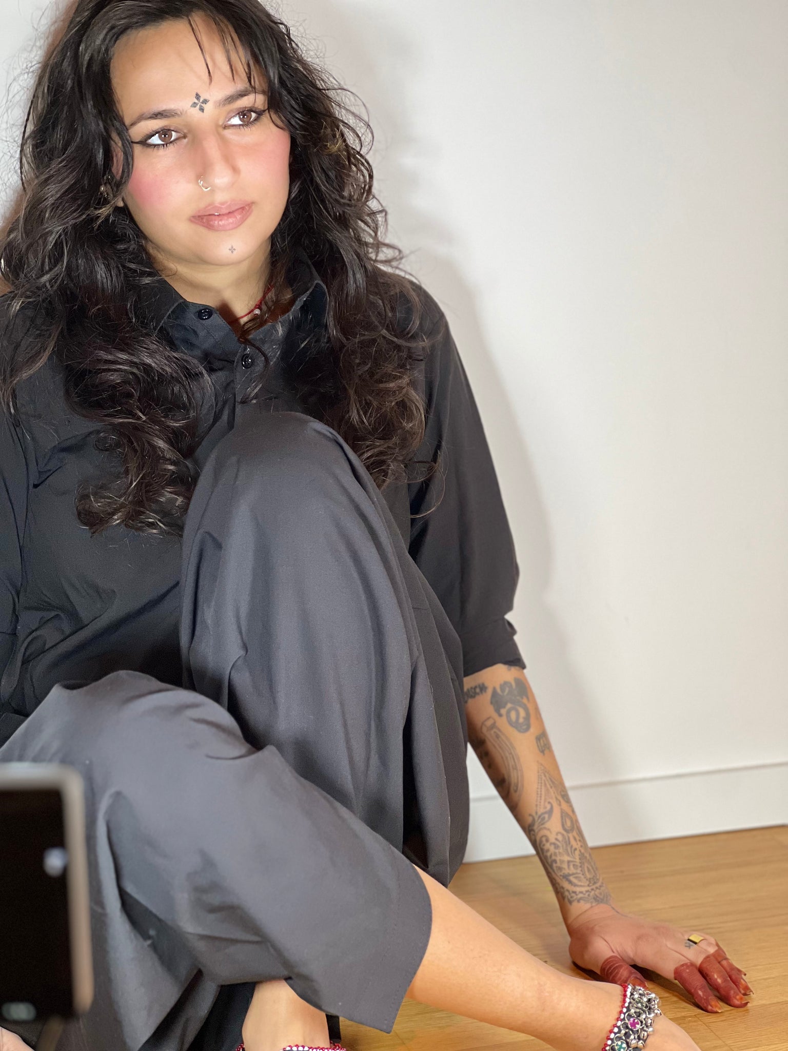 Woman in Afghan clothing looking away from the camera, a light near her crossed legs. 