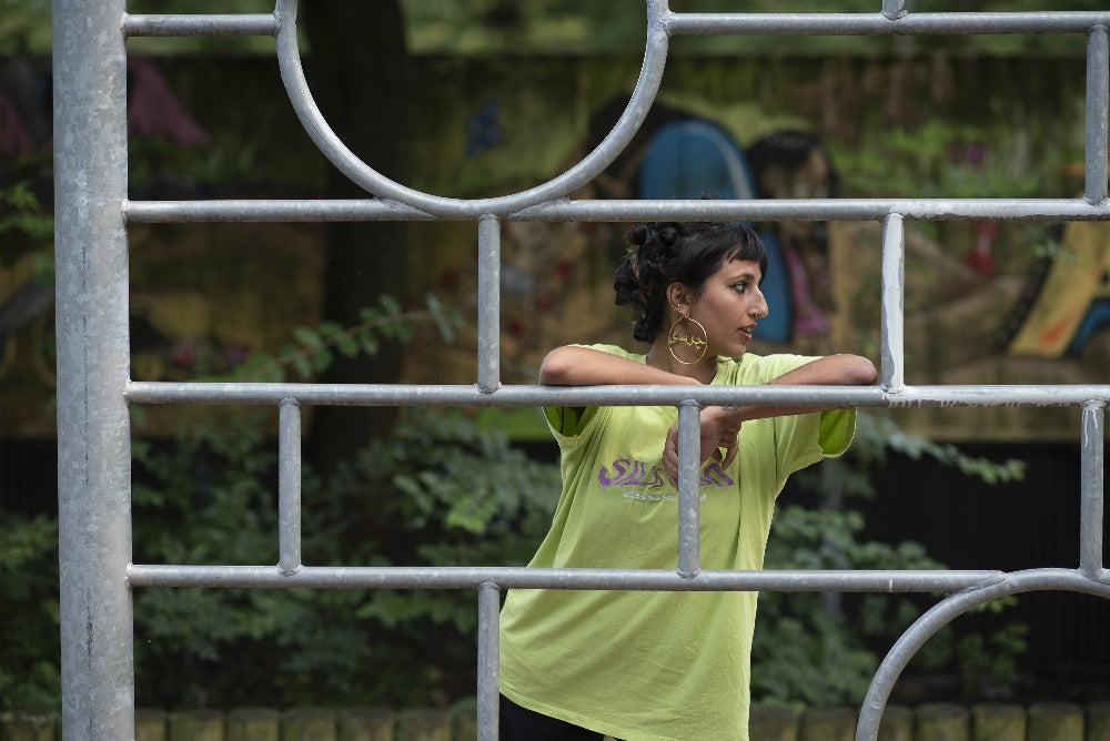 A woman, turned away from the camera, in a green tee shirt and big gold hoops on a playground.