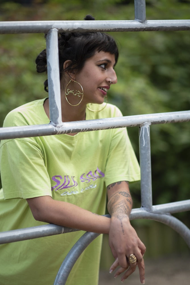 A woman, turned away from the camera, in a green tee shirt and big gold hoops on a playground.
