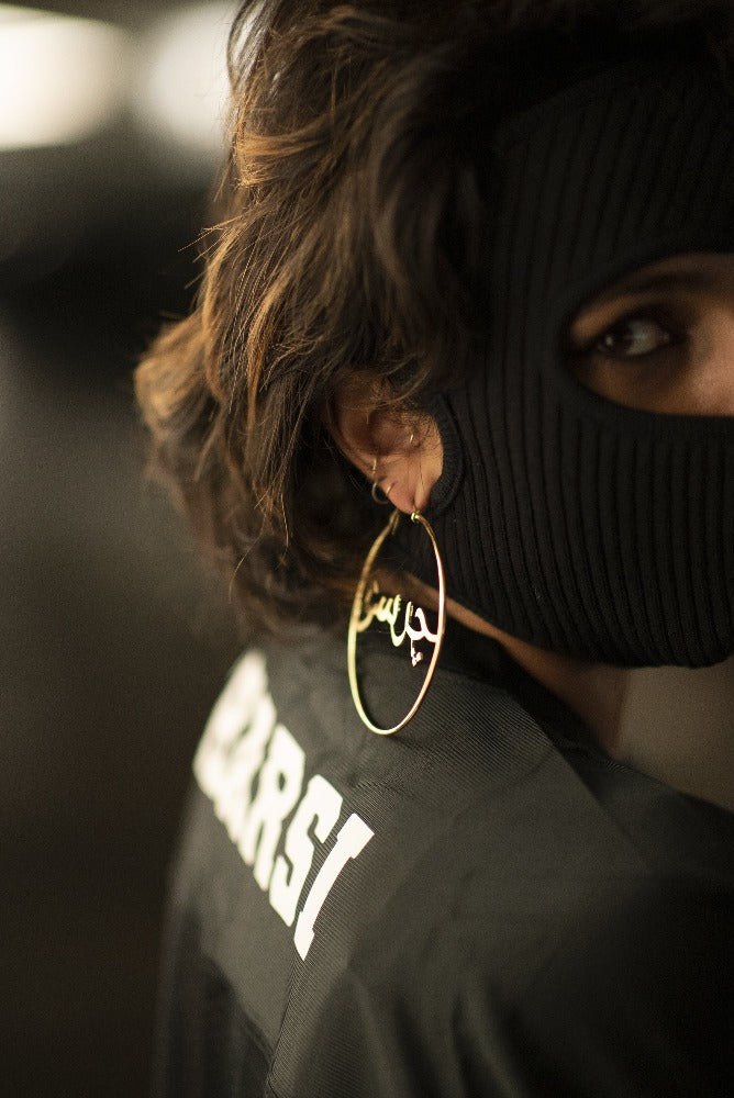 side photo of the back of a woman's jersey that reads "Charsi" in Latin script, wearing gold hoops.