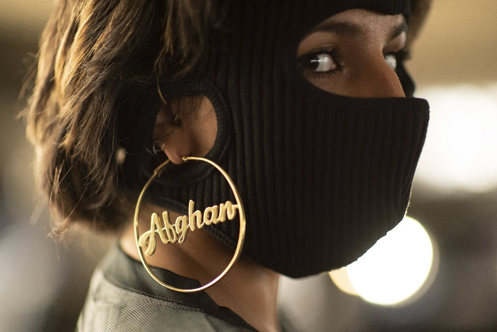 woman looking towards camera with a balaklava and gold hoops that say Afghan
