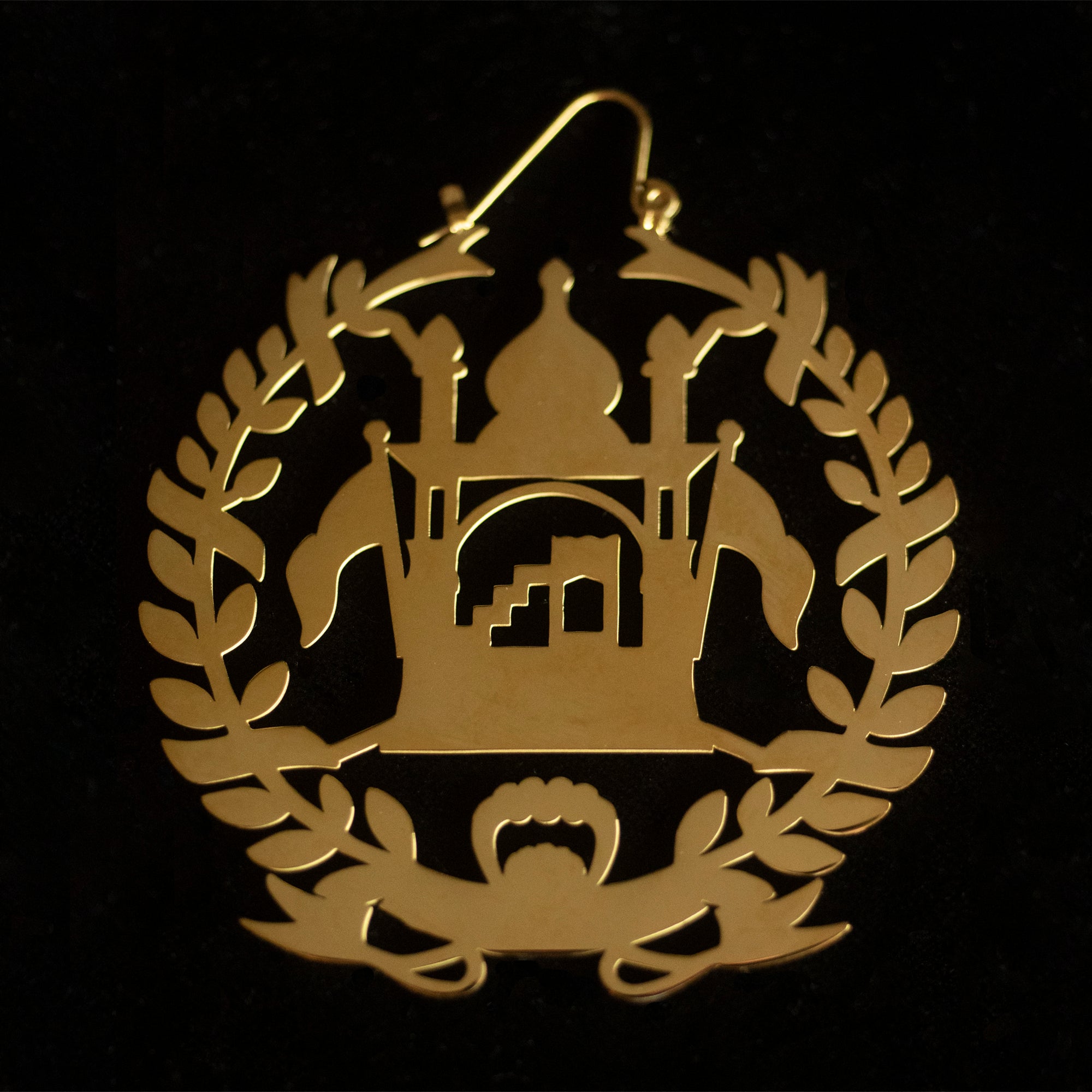 Earrings shaped as the mehrab of Afghanistan in gold against a black background.
