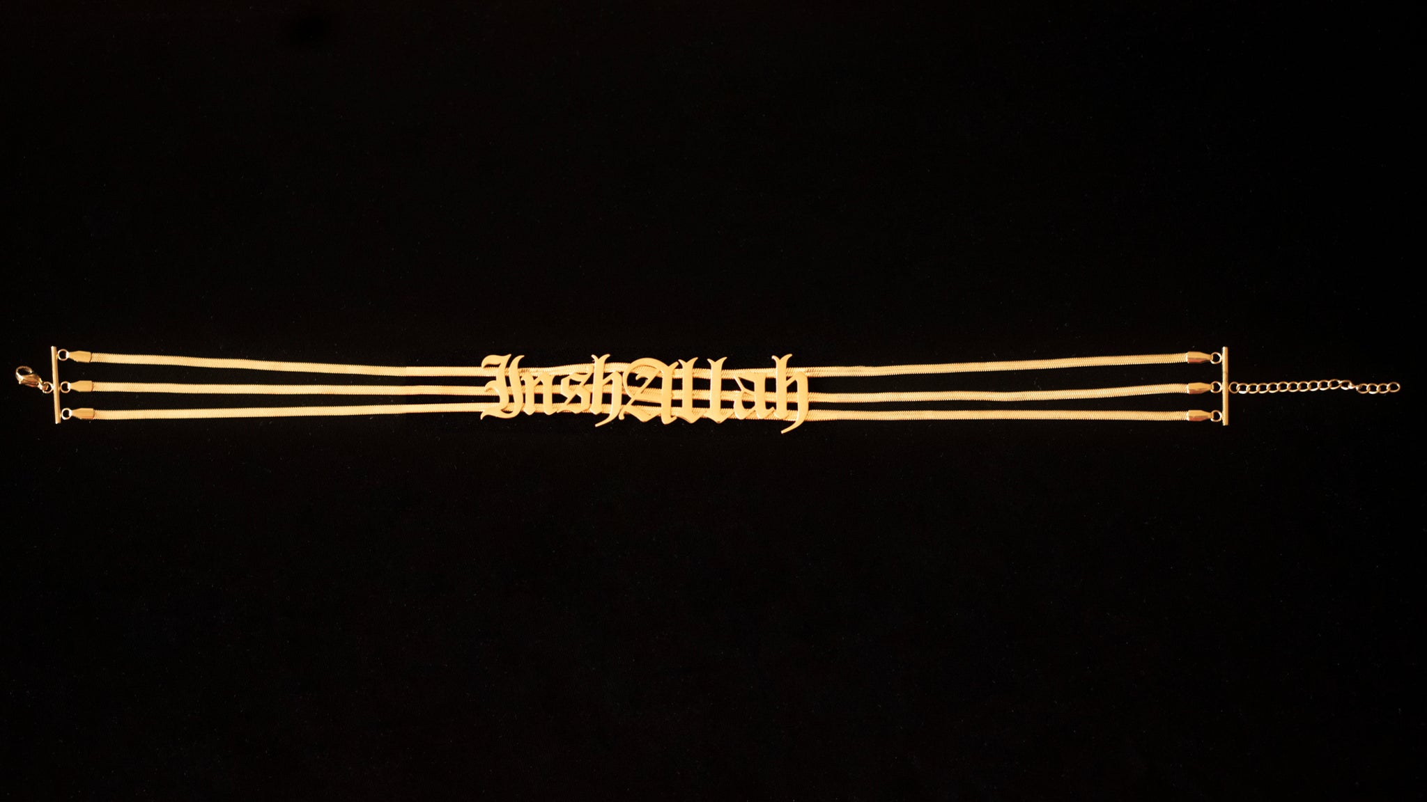 Against a black back drop sits a gold choker chain with the word InshAllah written on it.