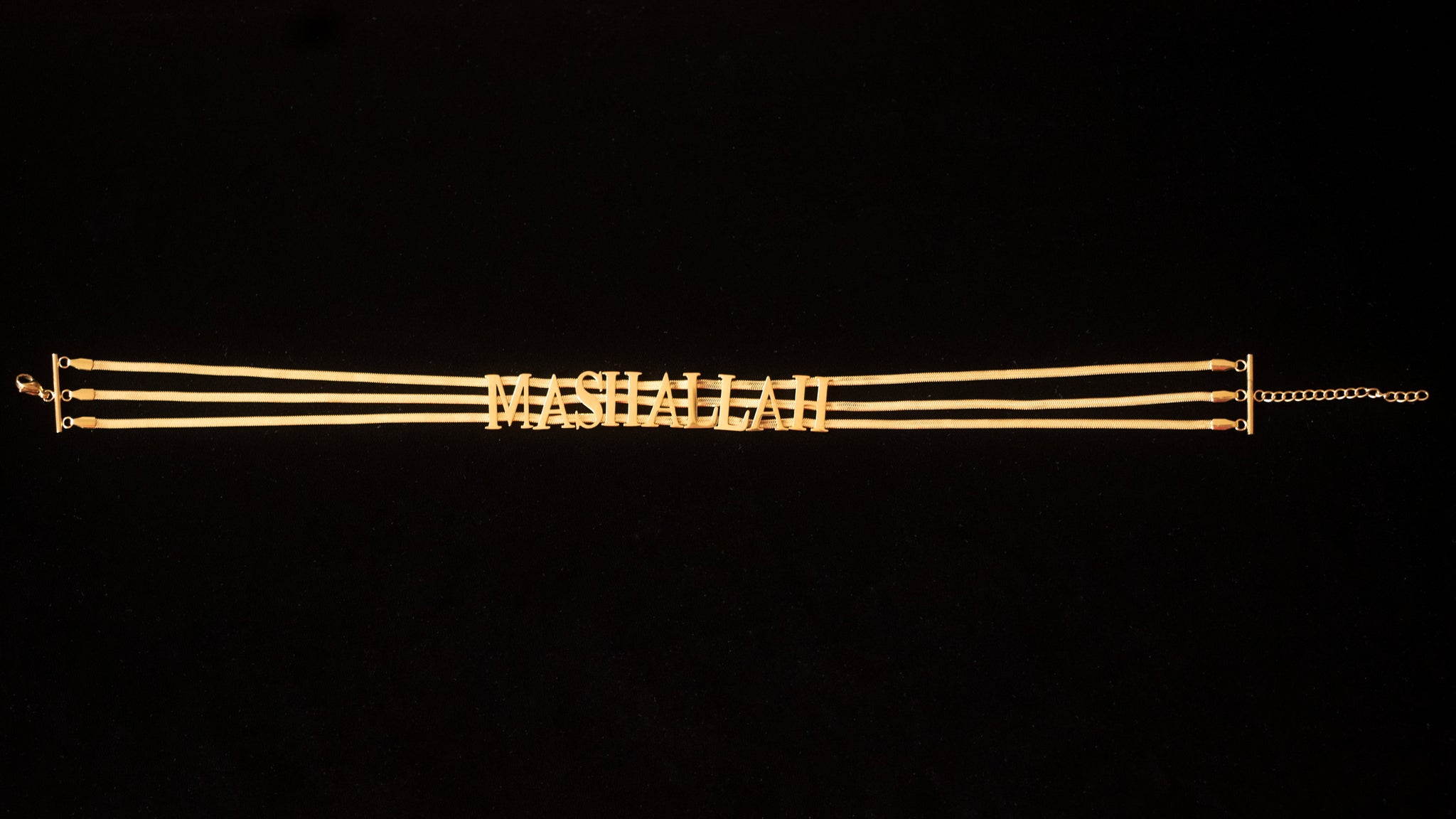 Against a black back drop sits a gold choker chain with the word MASHALLAH written on it.