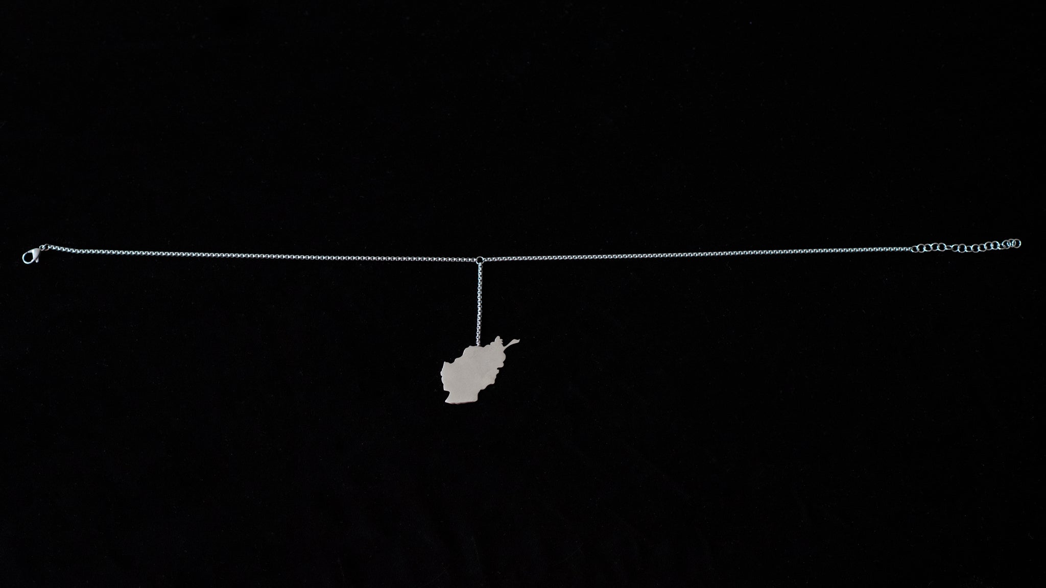 A map of Afghanistan hangs off a silver choker against a black backdrop.