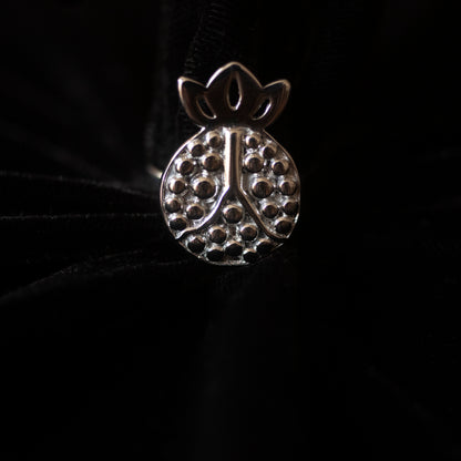 Against a black backdrop sits a pomegranate shaped silver ring.