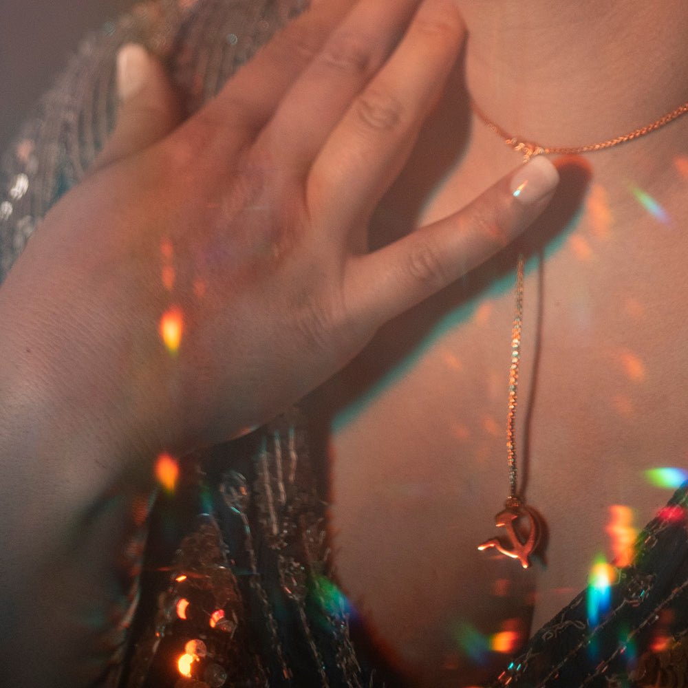 Person in a sequin dress wearing a hammer and sickle necklace with their hand by their chest.