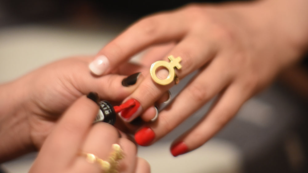 Person painting someone's hand with red nail polish, while wearing the venus la femme ring on their index ring.