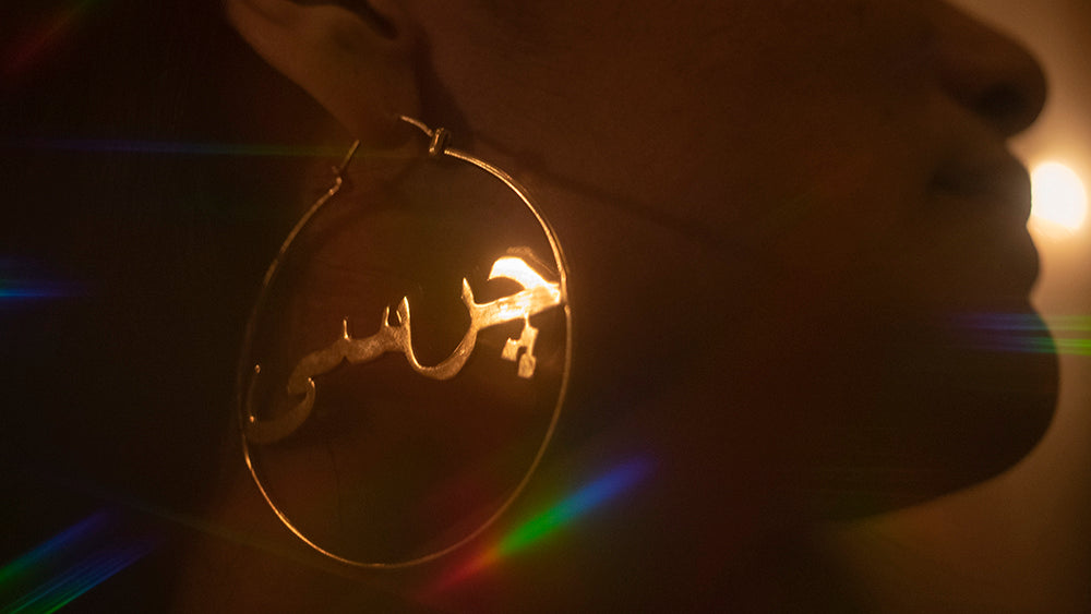 woman wearing hoop earring with 'charsi' written in the middle, green and holographic colors in the back.