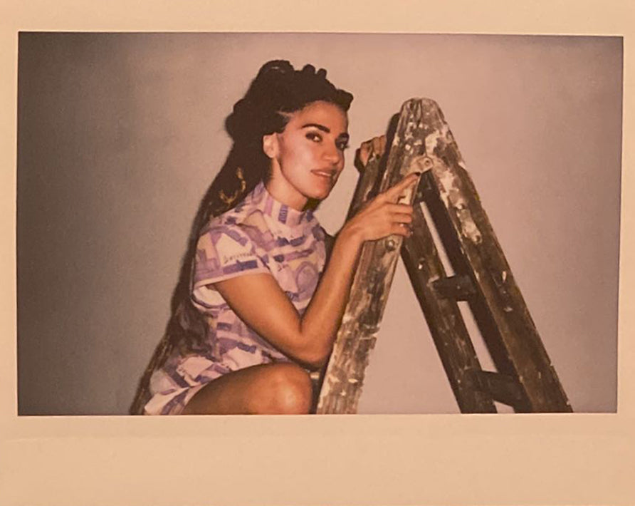 A polaroid of a woman on a ladder smiling.