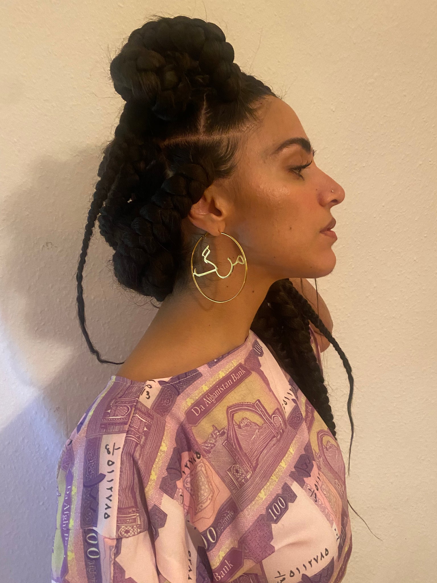 A woman with braids profile while she wears gold hoops with the word 'marg' in the middle.