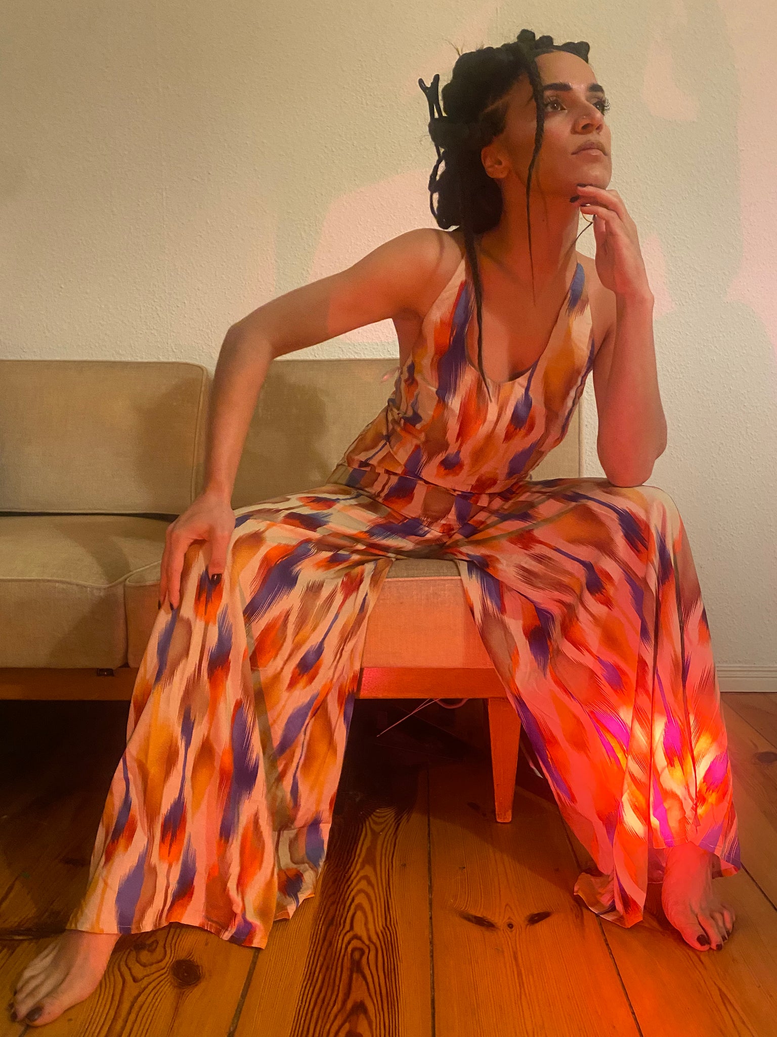 A woman leans over on a yellow couch, her colourful clothes matching the couch and the red light shining on her.