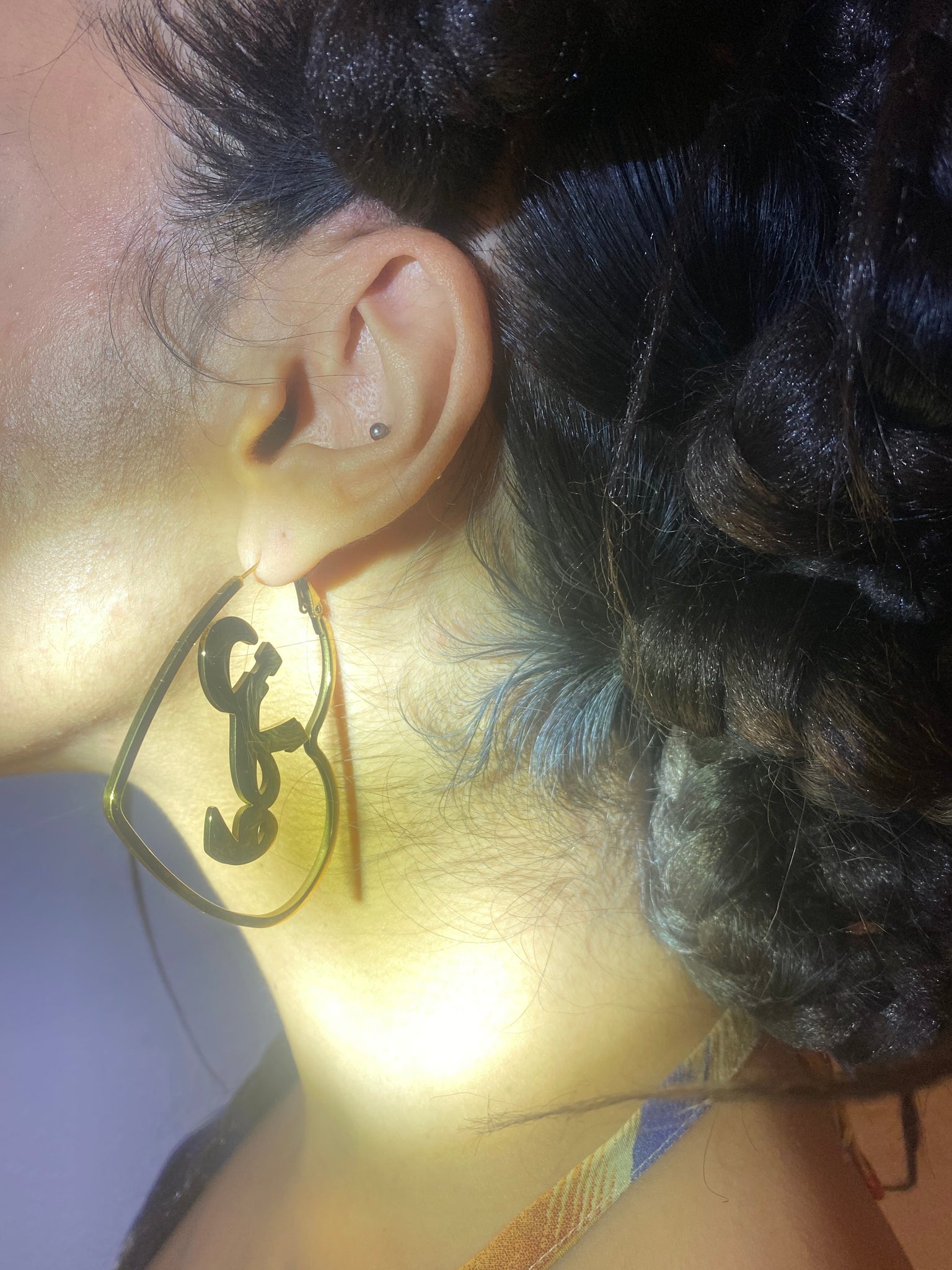 A woman's ear wearing gold watan heart hoops