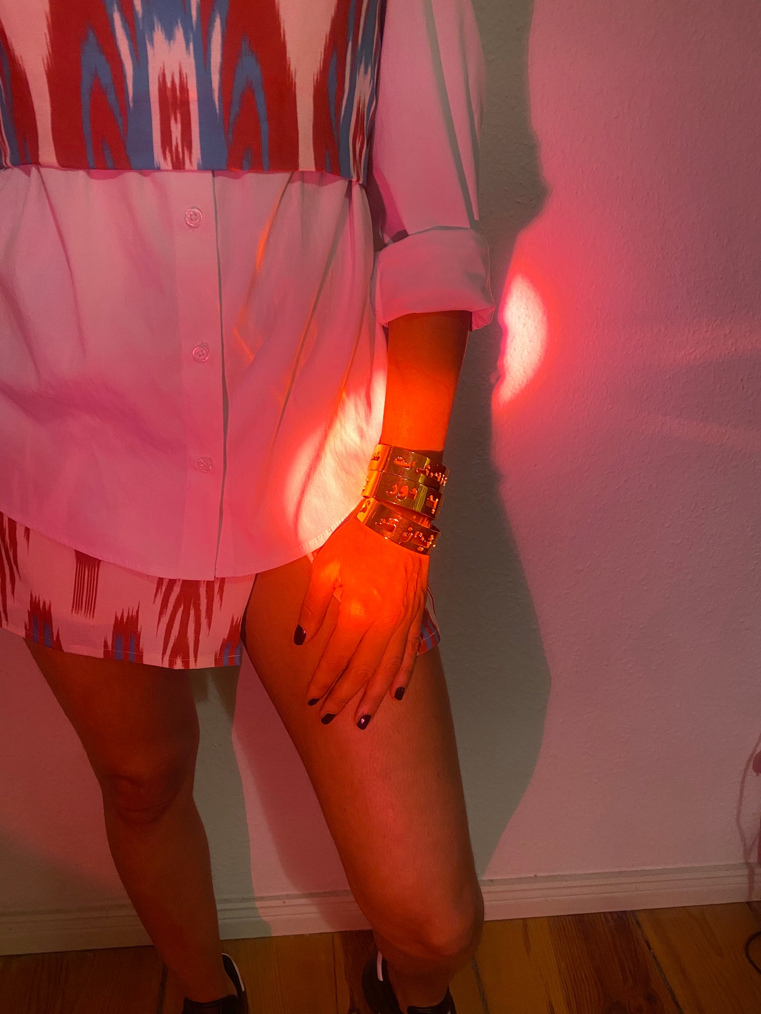 A red light focuses on a woman's arm with three gold bangles on it.
