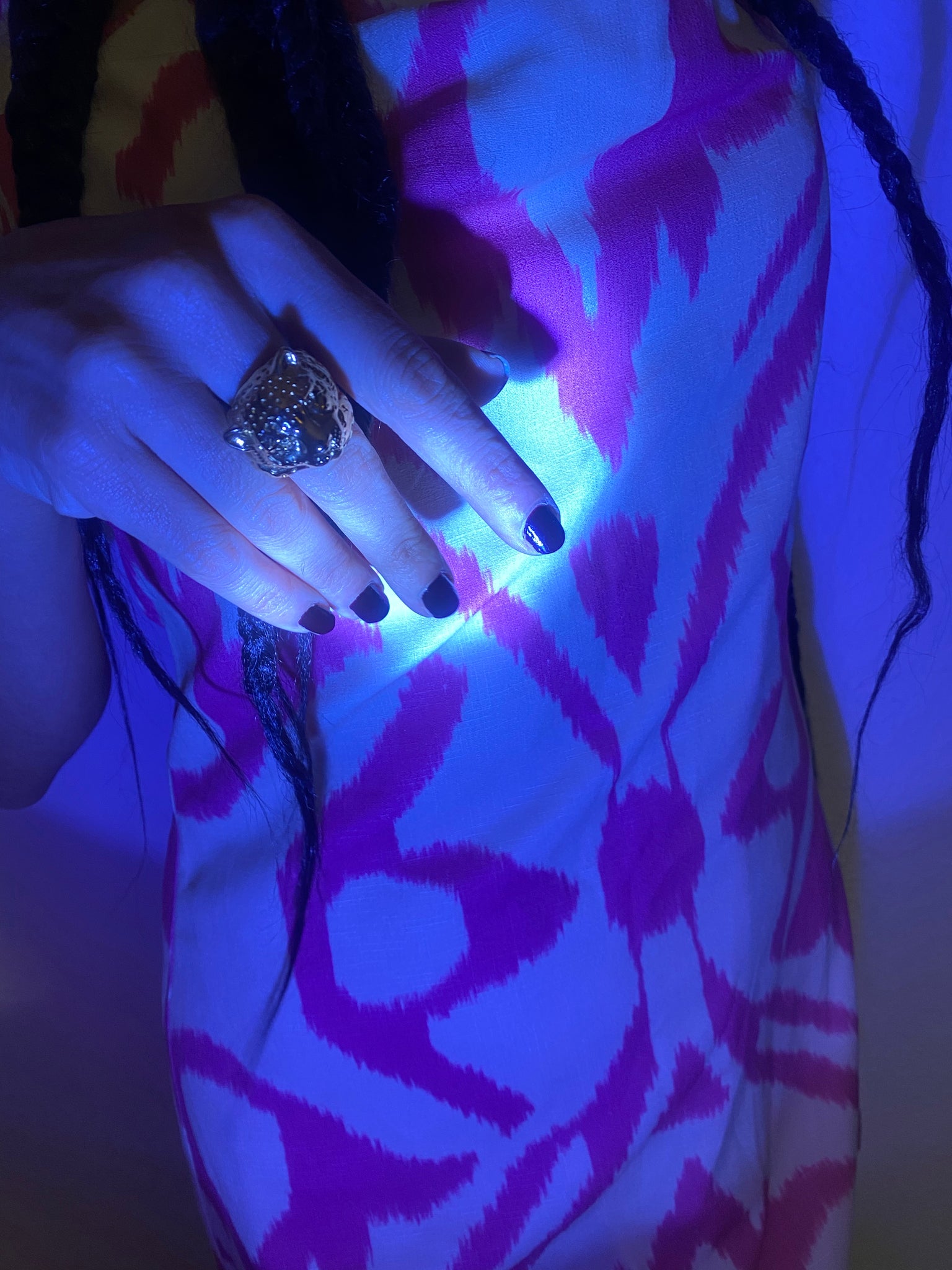With moody blue lighting, a woman holds up her hand wearing a gold snow leopard ring and wearing an adras dress.