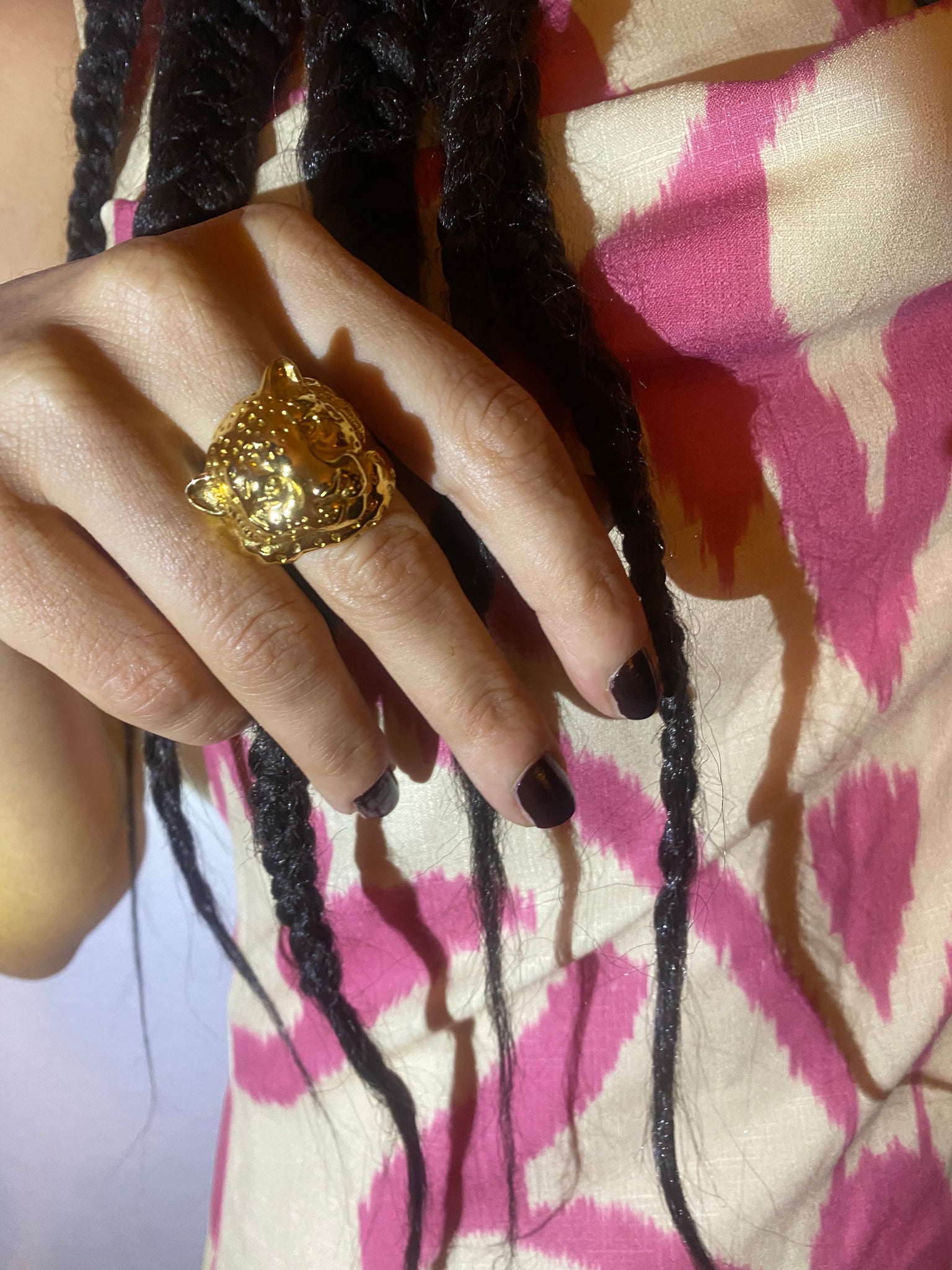 A woman holds up her hand wearing a gold snow leopard ring and wearing an adras dress and long braids.