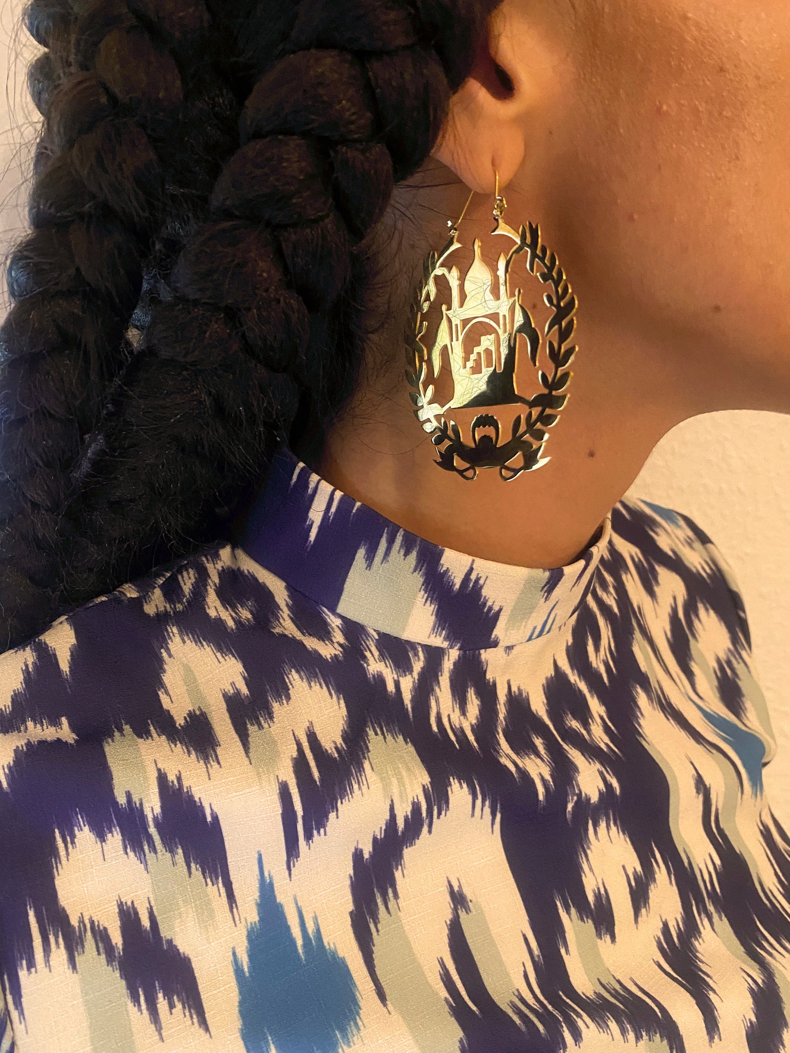 A woman with long braids wears gold mehrab earrings reflecting light.