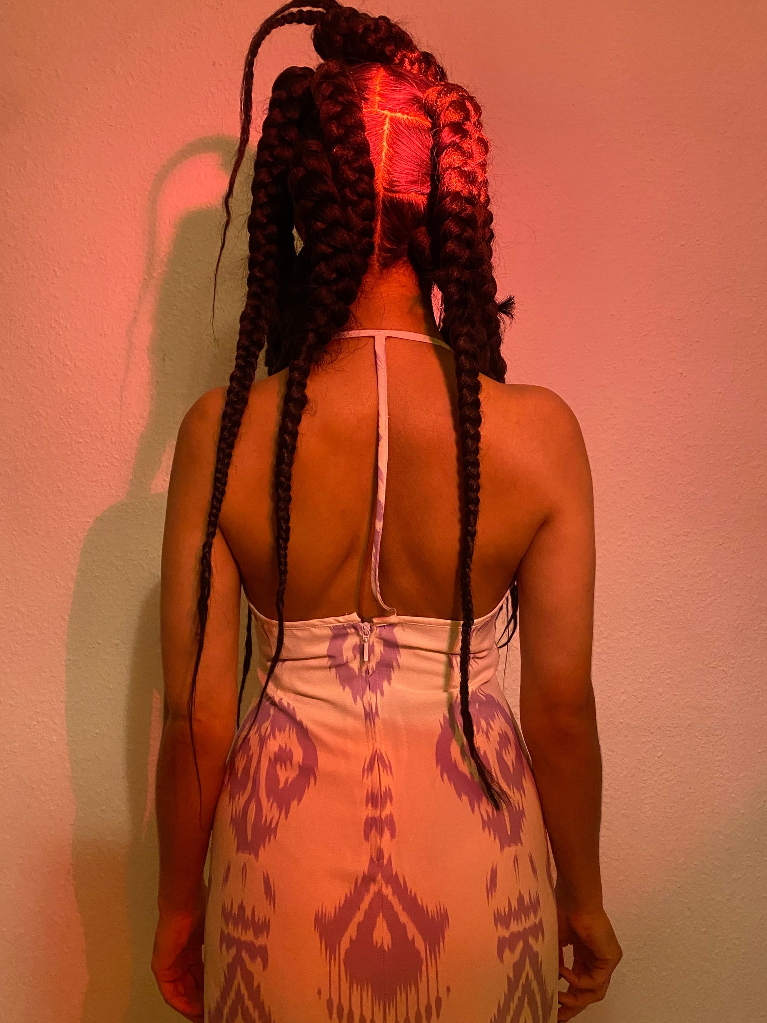 A woman with braids back wearing a white and lavender adras dress.