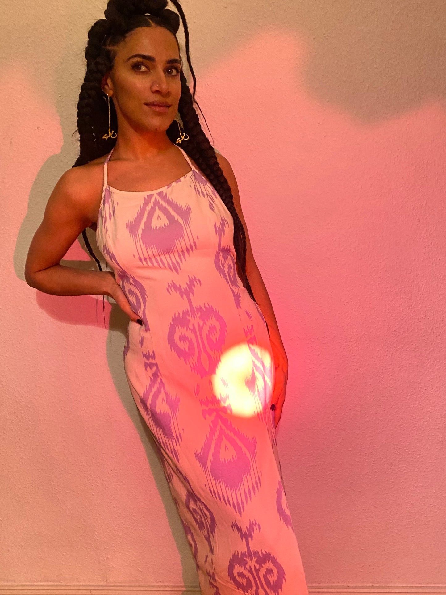 A woman wearing a dress with long braids and gold earrings hanging from her ears.