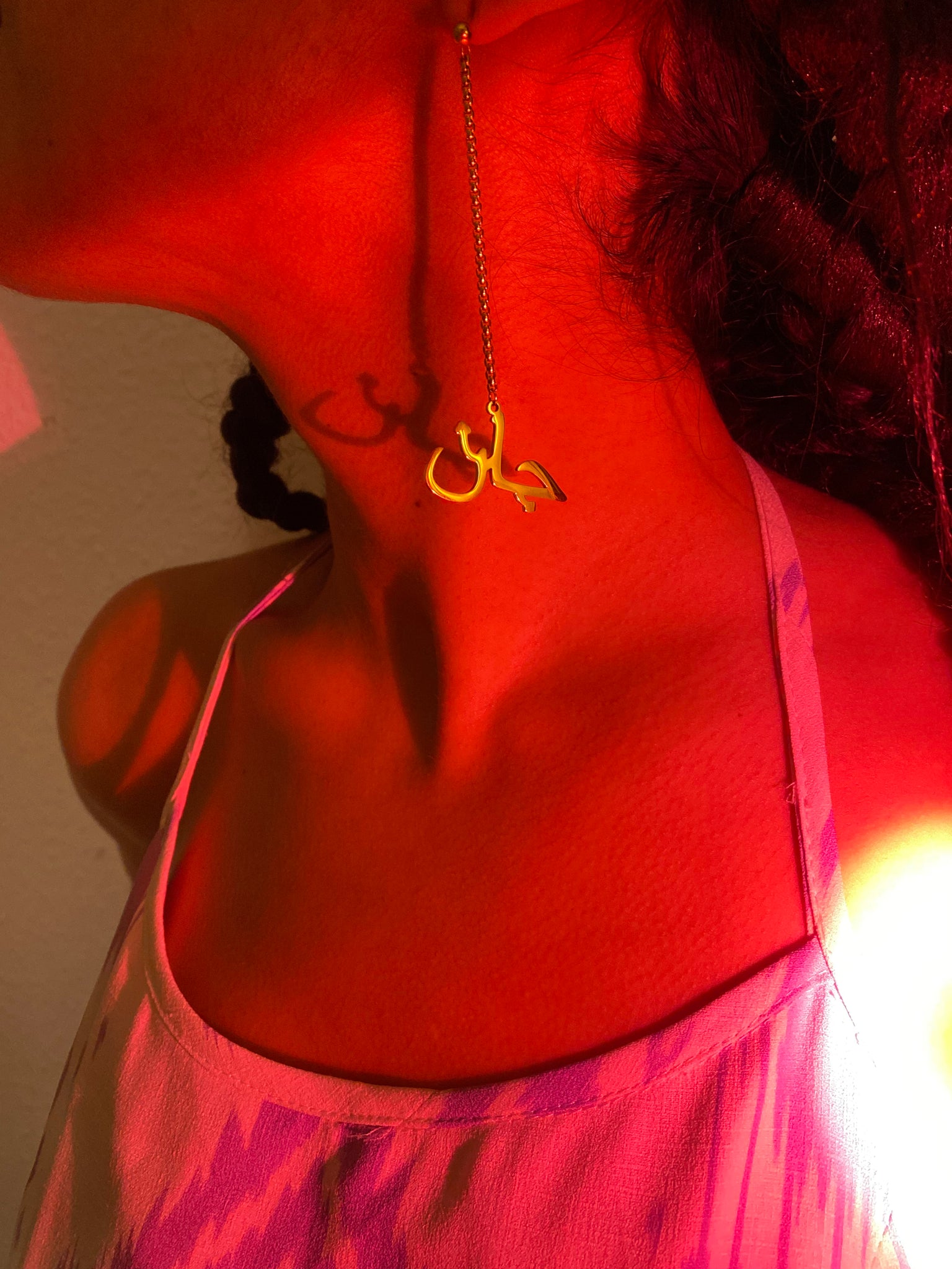 A close up of a woman's ear wearing dangly earrings with the word 'jaan' against red lighting reflecting.