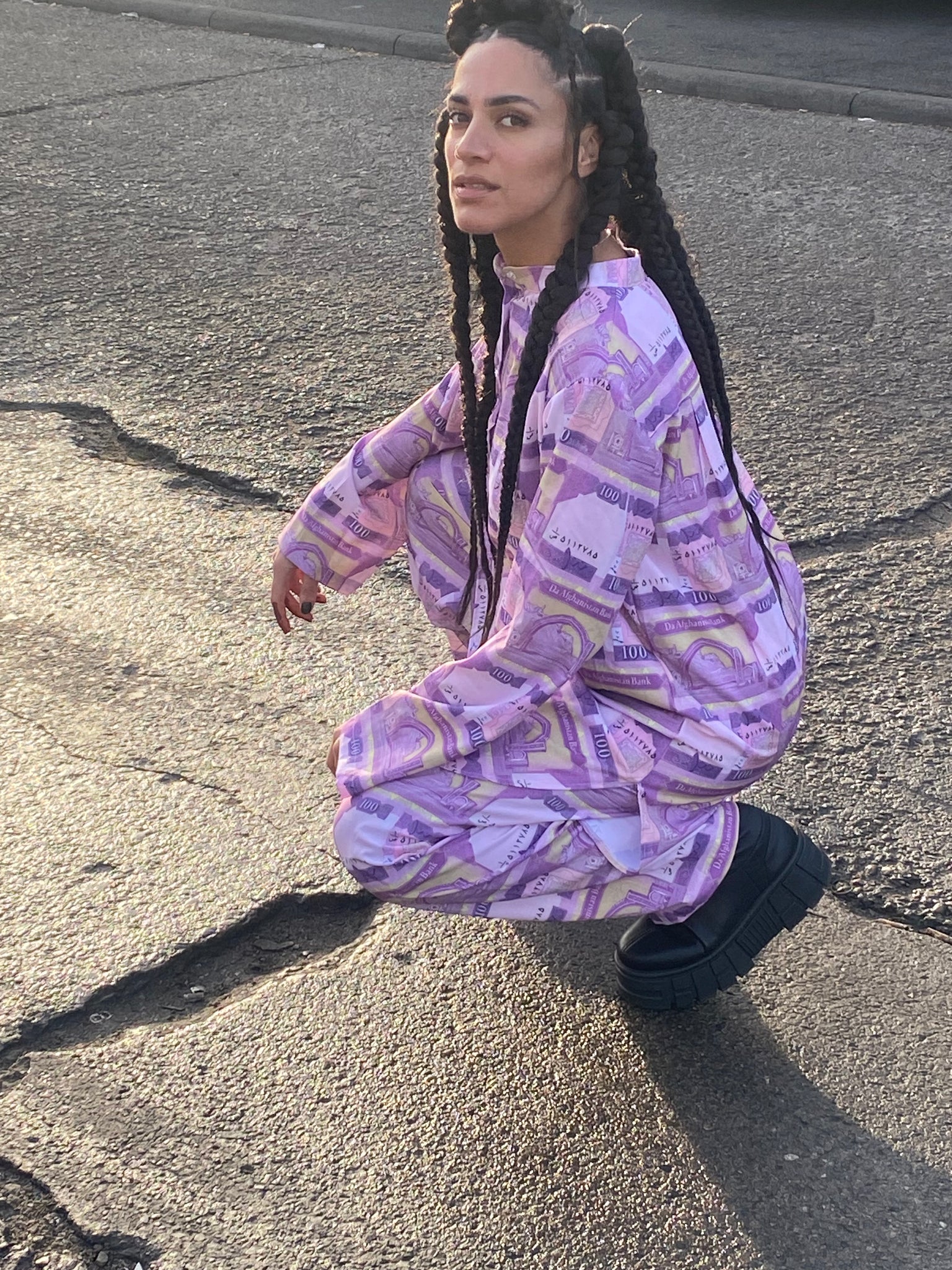 A woman with braids squatting in a peran tunban made of 100 Afghani fabric.