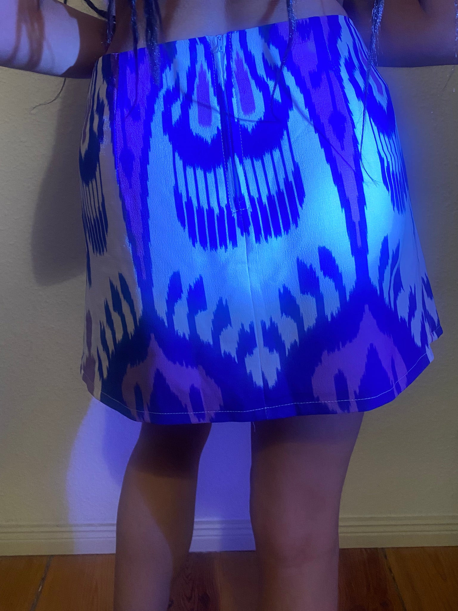 A blue light shines on Uzbeki fabric and the zip closure of the mini skirt.