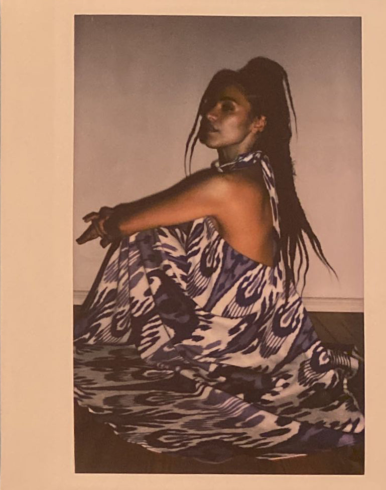 A polaroid of a woman in a long flowing dress sitting on the ground.