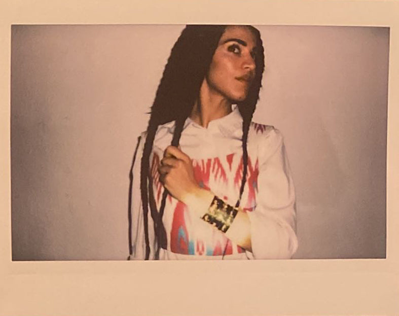 A polaroid of a woman with braids and an ikat outfit has three gold bangles that shine.