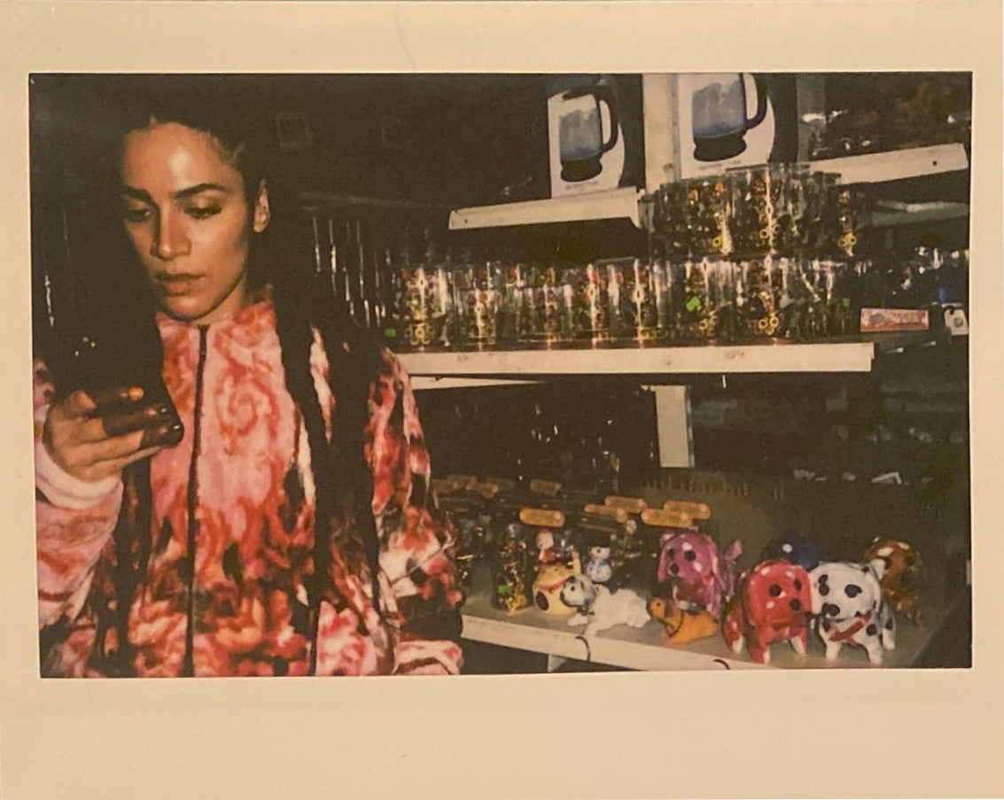 Woman on phone with henna-ed hands in front of toys in a red blanket jacket.