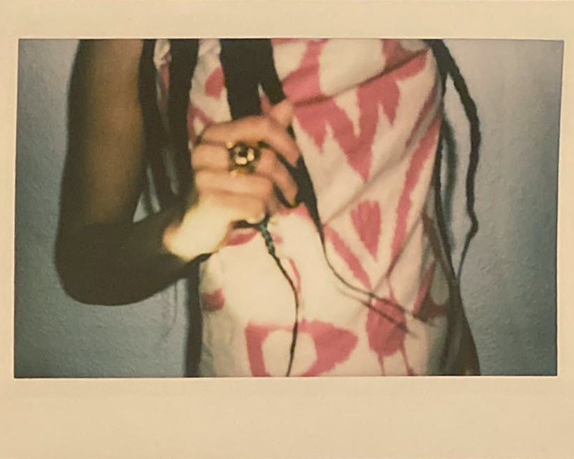 Polaroid of a hand holding braids, a full person not seen but wearing uzbeki adras.