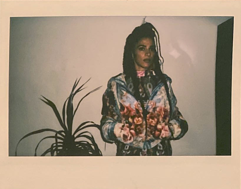 Polaroid of woman next to a plant and light blue fuzzy blanket jacket.