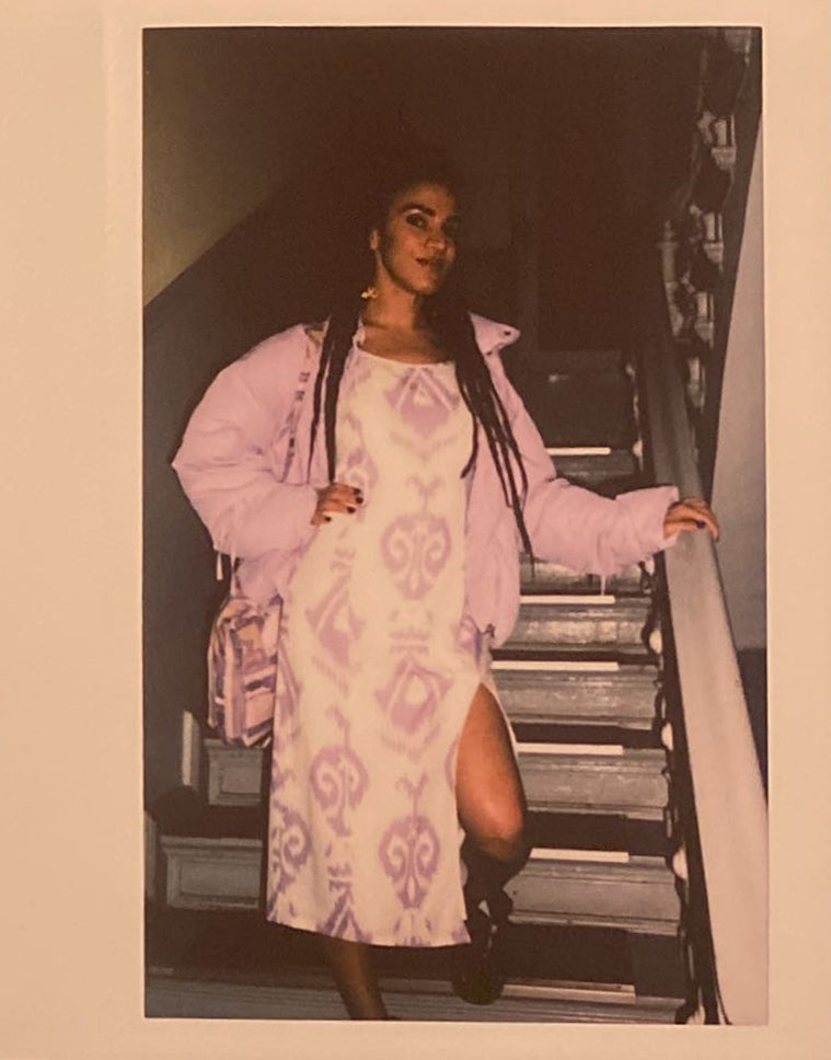 A polaroid of a woman on a staircase, wearing a dress with a leg slit.