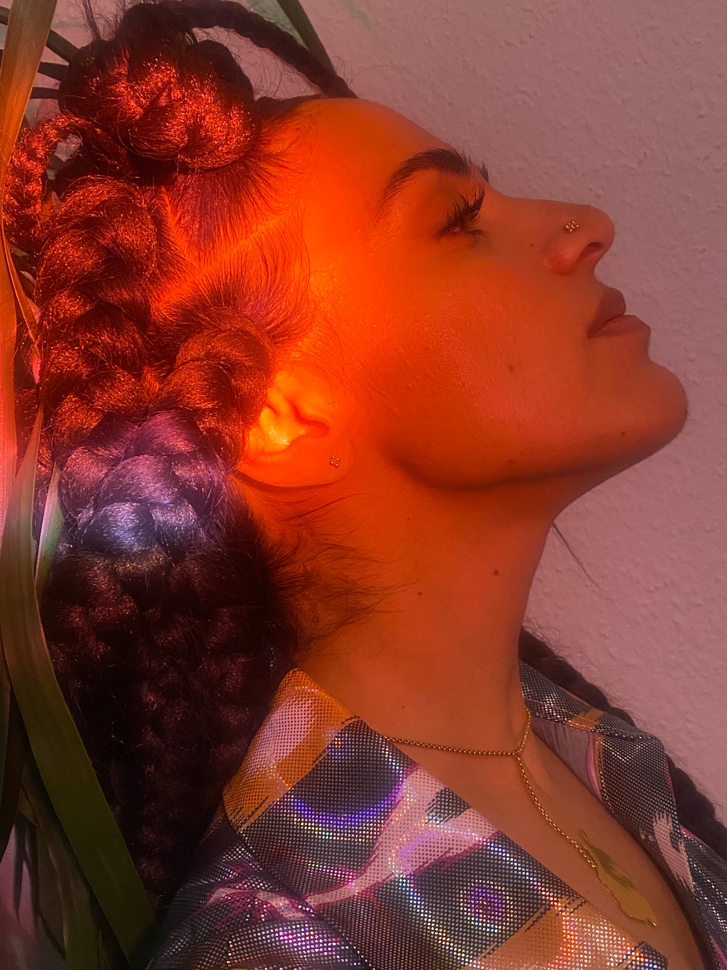 A woman with braids leans back, a gold nose stud in her nose.