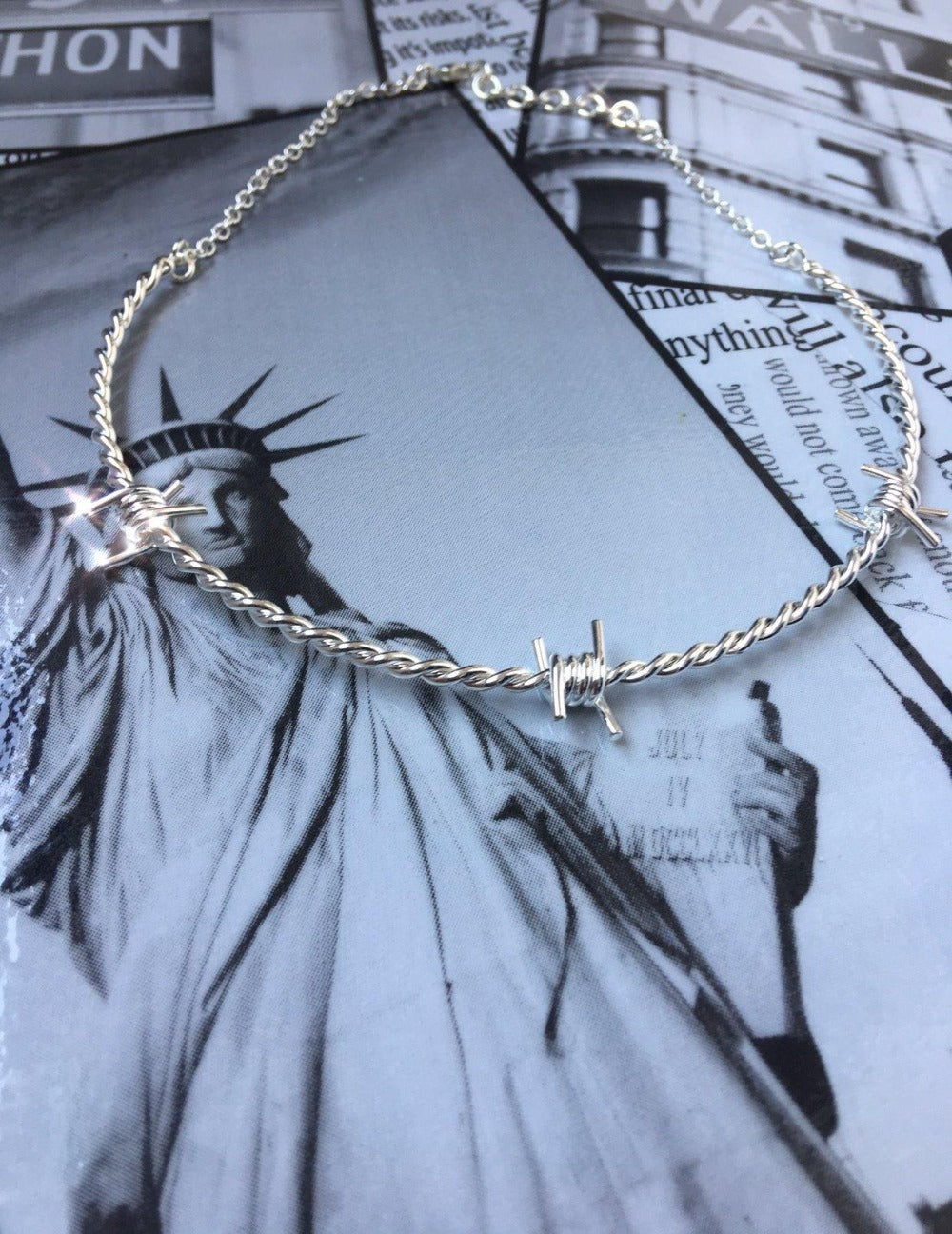 The Kabul House Essential Barb Wire Choker - Blingistan, silver barbwire necklace on statue of liberty print.