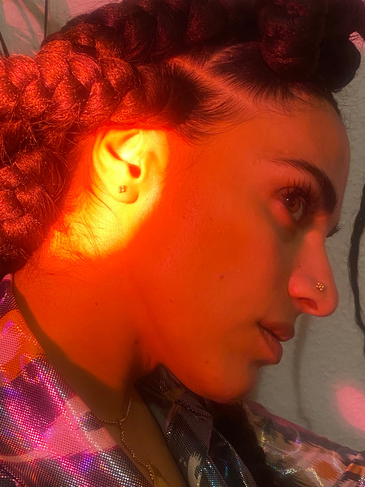 A woman with braids leans forward with a gold stud in her nose and ear.