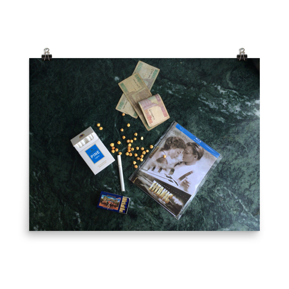 Afghani money, pine cigarettes, chickpea nuts, matches and a blue ray disk or Titanic on a green marble background print, hung on two clips.