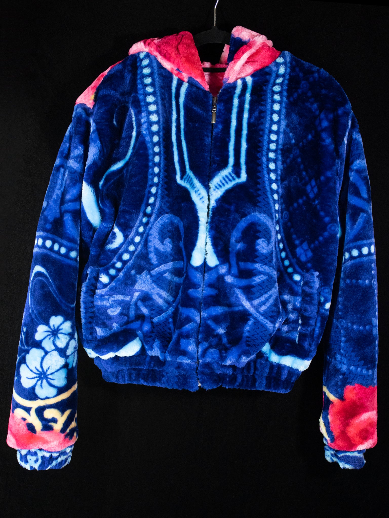 A blue and pink jacket hangs on a hanger against a black backdrop.