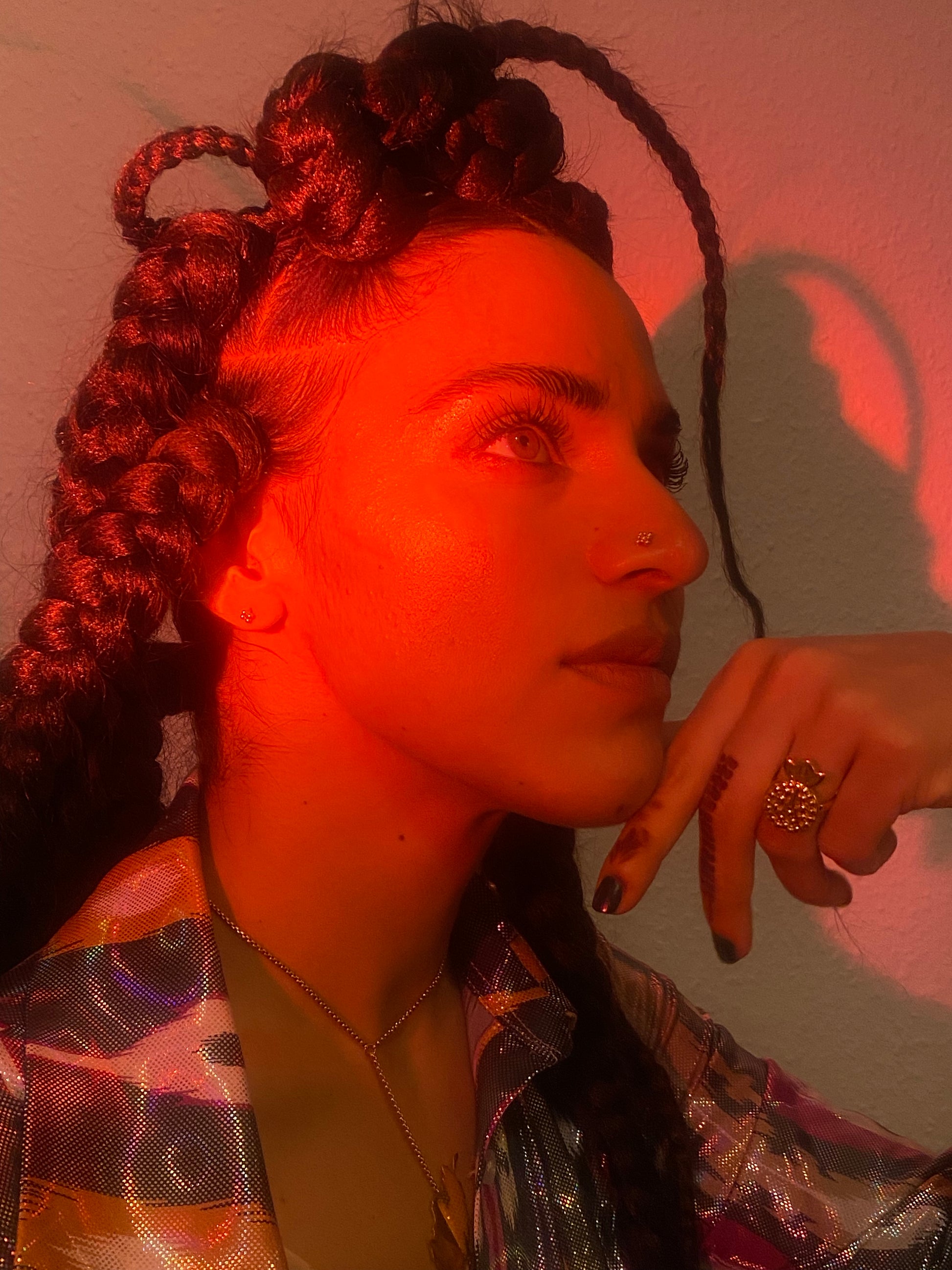 A woman wears a pomegranate shaped ring in gold with a moody red lighting on her. 
