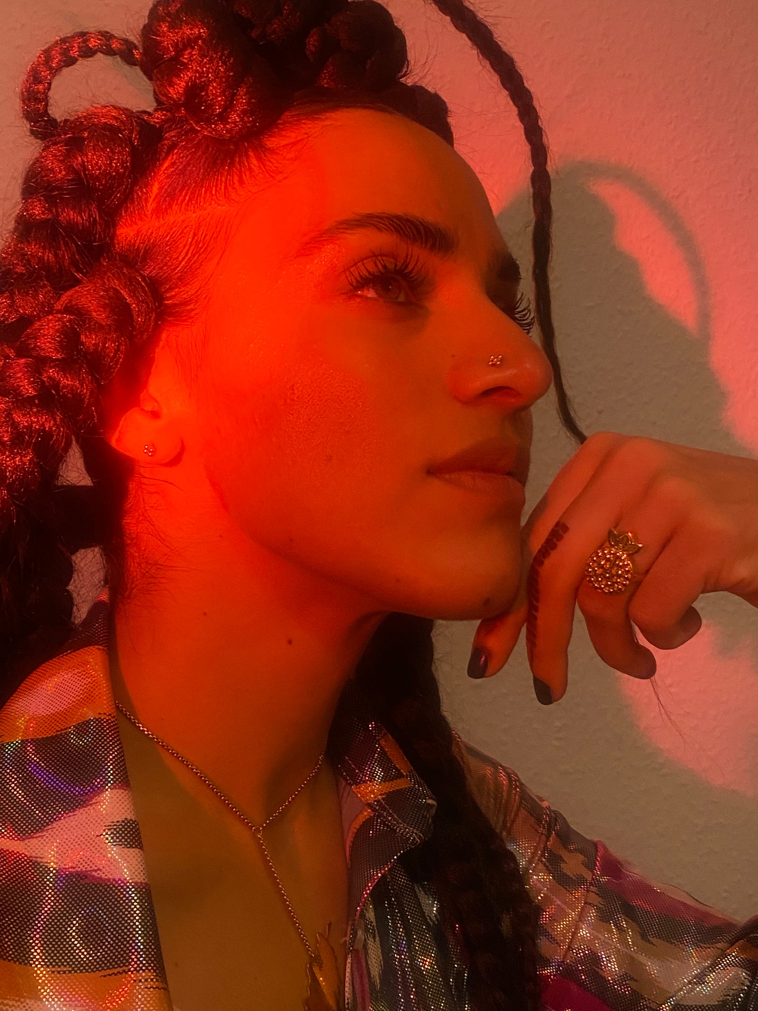 A woman looks up with gold jewellery under red lighting.