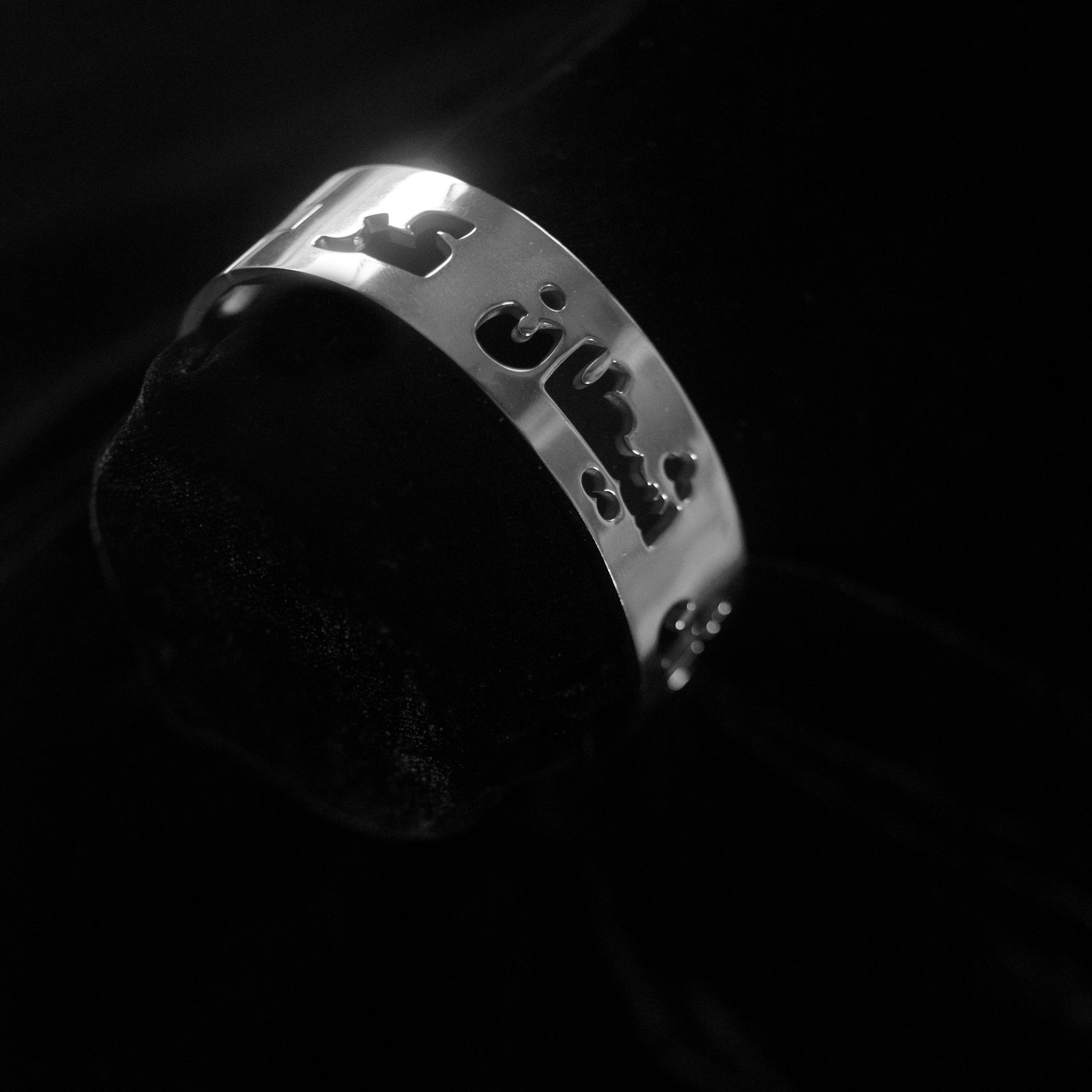 A silver bangle that says Gosh Shaitan Kaar in Dari against a black background.