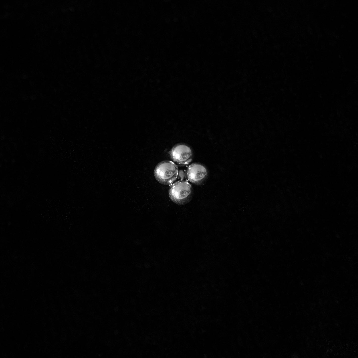Silver small stud earring against black background in a sheenkhaal tribal tattoo style.
