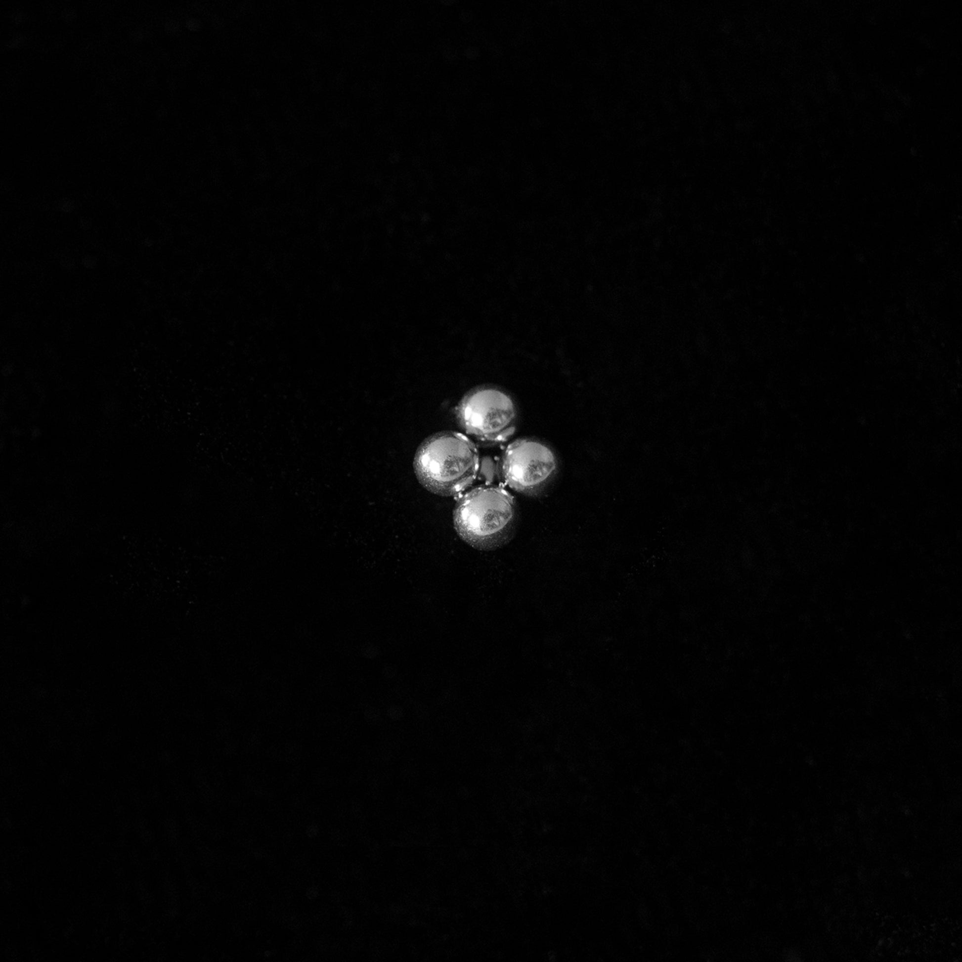Silver small stud earring against black background in a sheenkhaal tribal tattoo style.