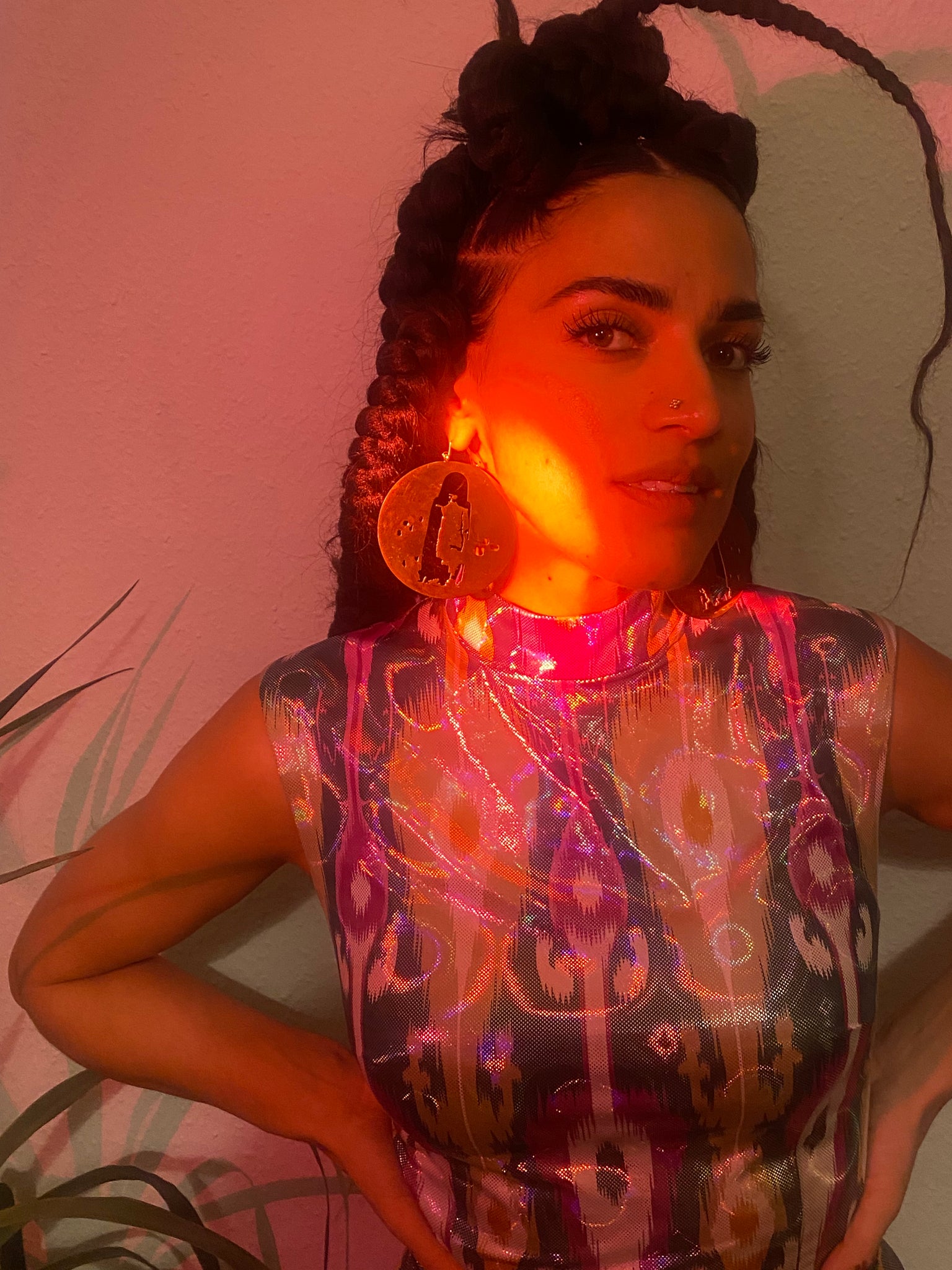 A red light shines on a woman with braids whose gold Buddha hoops catch the light.