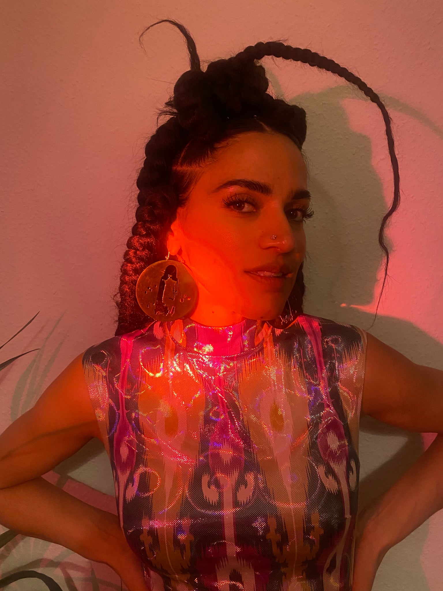 A woman with braids and hoops smiles at the camera, red light shining on her face.