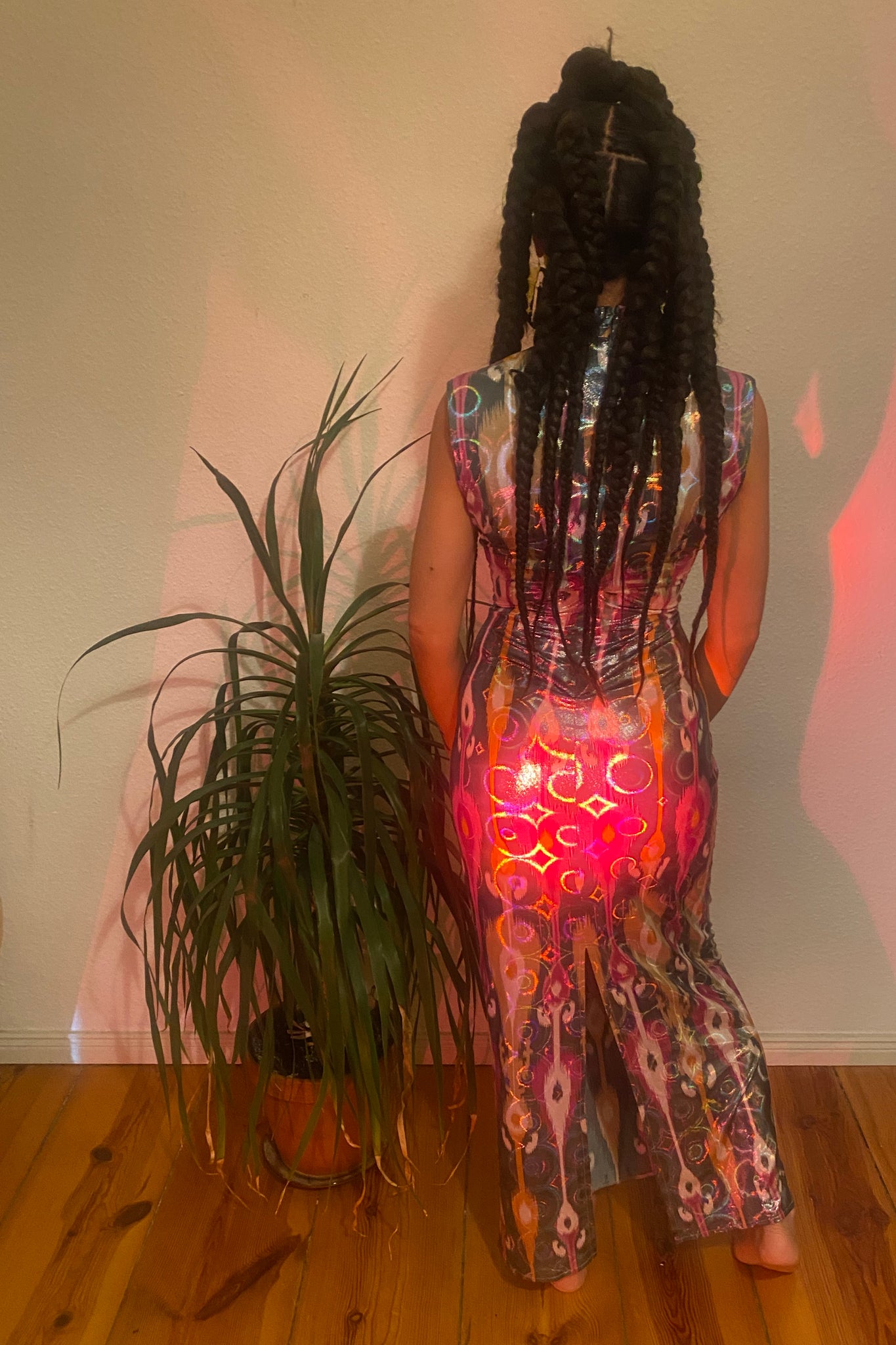 A woman's back side next to a plant wearing a colourful adras/ikat dress.